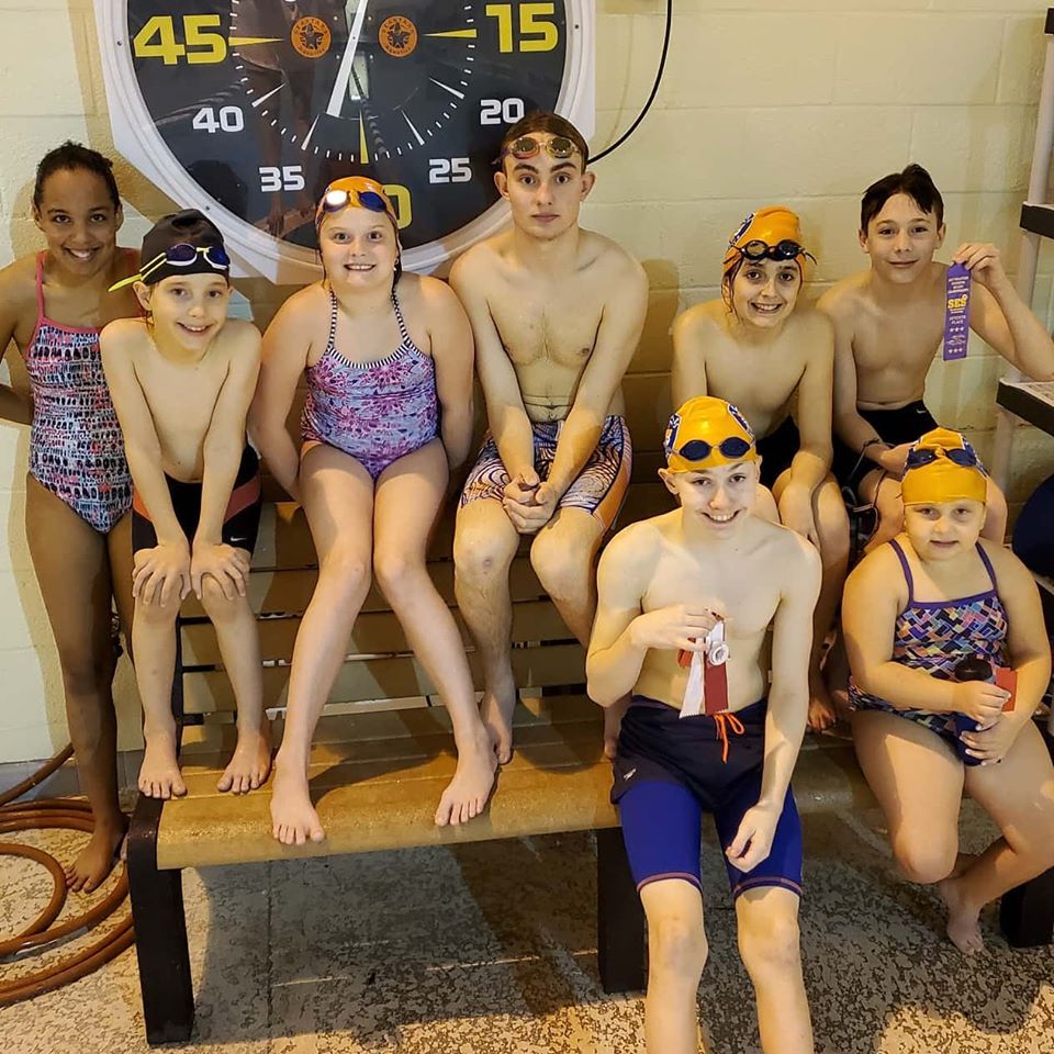 Swim team posing with ribbons and trophies.