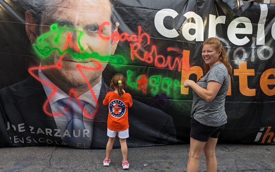 Two children stand in front of a colorful protest banner about care reform.