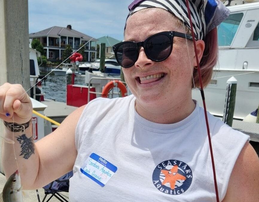 Smiling woman in sunglasses and headscarf holding a fish on a boat.